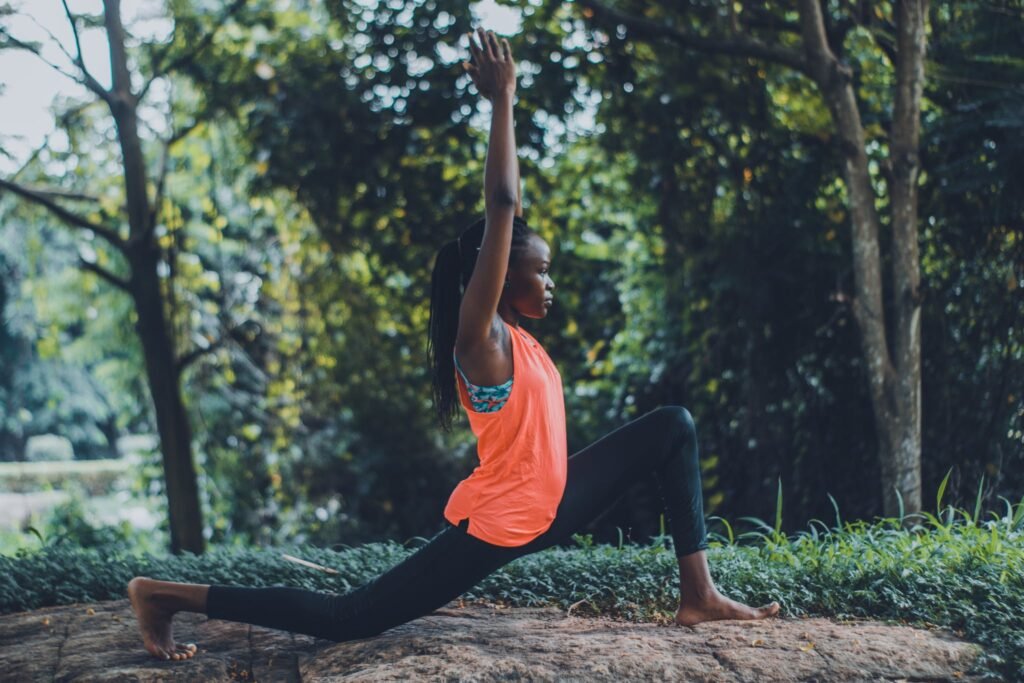 Photo of Woman in Orange Tank Top and Black Pants Striking a Yoga Pose Outdoors at one of the yoga retreats in South Africa.