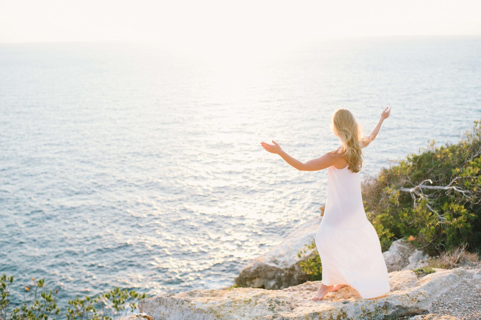 A woman in a white dress standing on a cliff overlooking the ocean while on one of these Algarve retreats.