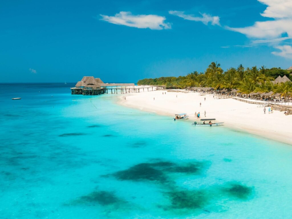 An aerial view of a beach in Zanzibar with a resort in the background and boats taking passengers to Zanzibar snorkeling spots.