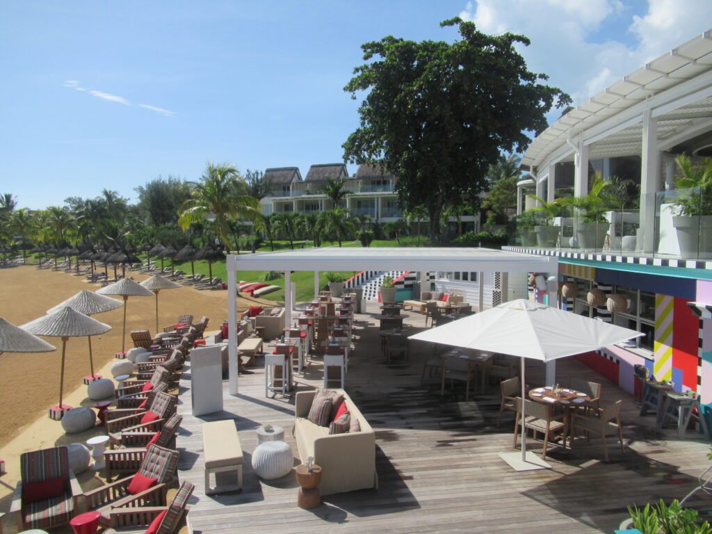 A large deck by the beach filled with tables, chairs, umbrellas and more.