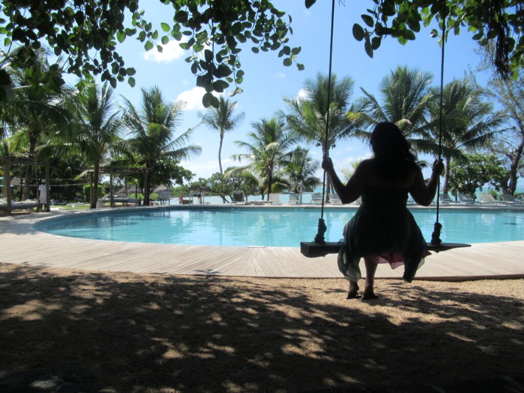 A silhouette of a woman in a flowy dress swinging in front of a pool in a tropical location.