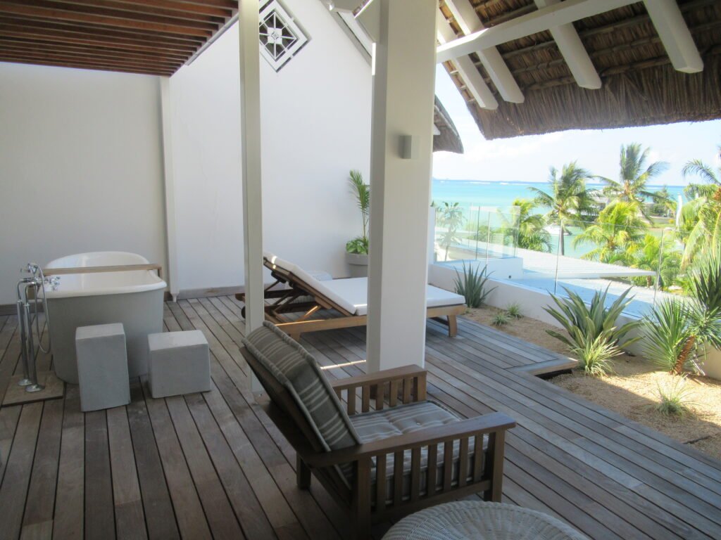 A wooden balcony with loungers, a seat, a bathtub and a sea view.