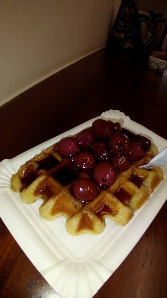 A Belgium waffle on a plate topped with cherries