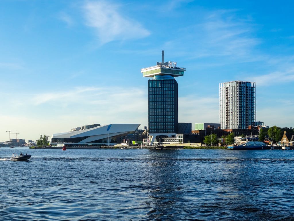 Explore the modern architecture of Amsterdam's skyline along the river with a boat in the foreground.