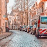Picturesque street scene in Groningen with parked bicycles and cars lining cobblestone road.