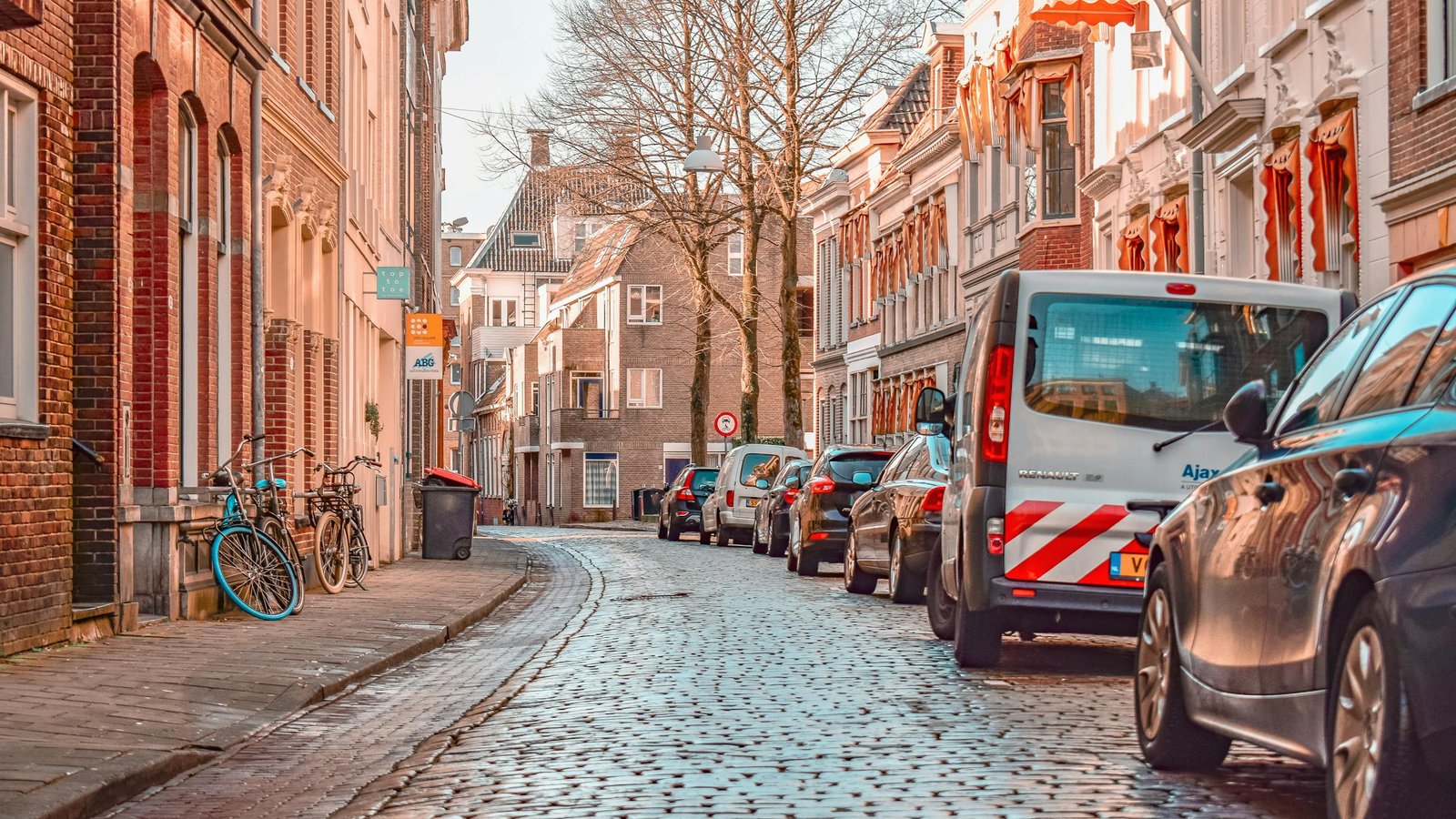 Picturesque street scene in Groningen with parked bicycles and cars lining cobblestone road.