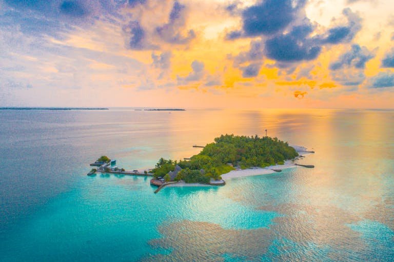 A breathtaking aerial view of a vibrant sunset over a tropical island in the Maldives, surrounded by turquoise waters.