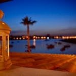 A serene evening view with a lit lantern, ocean, and palm silhouette in Algarve, Portugal.