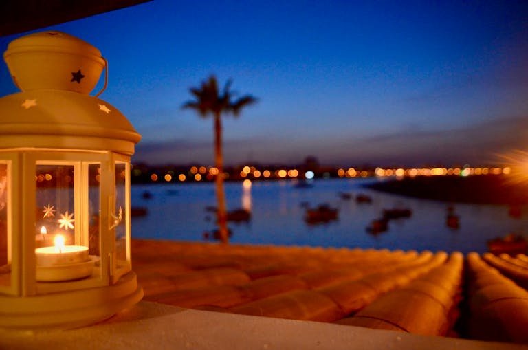 A serene evening view with a lit lantern, ocean, and palm silhouette in Algarve, Portugal.