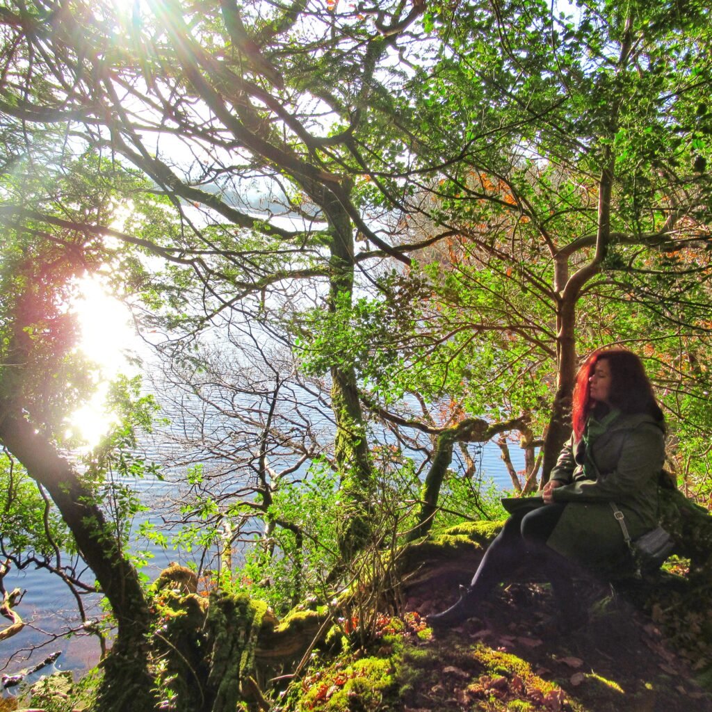A woman sitting peacefully in the forest by a loch in Ireland.