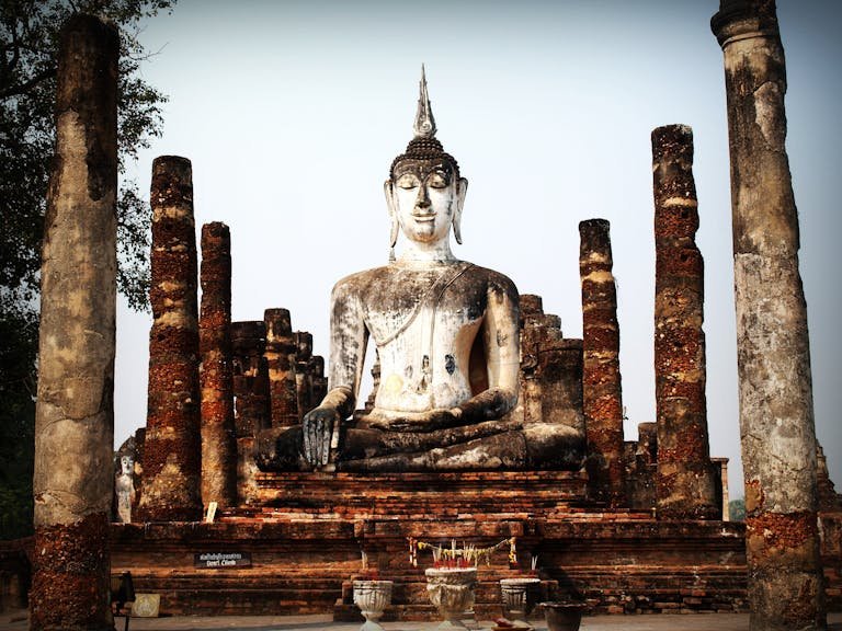 Serene Buddha statue surrounded by ancient pillars in Ayutthaya, Thailand, showcasing timeless beauty and cultural heritage.