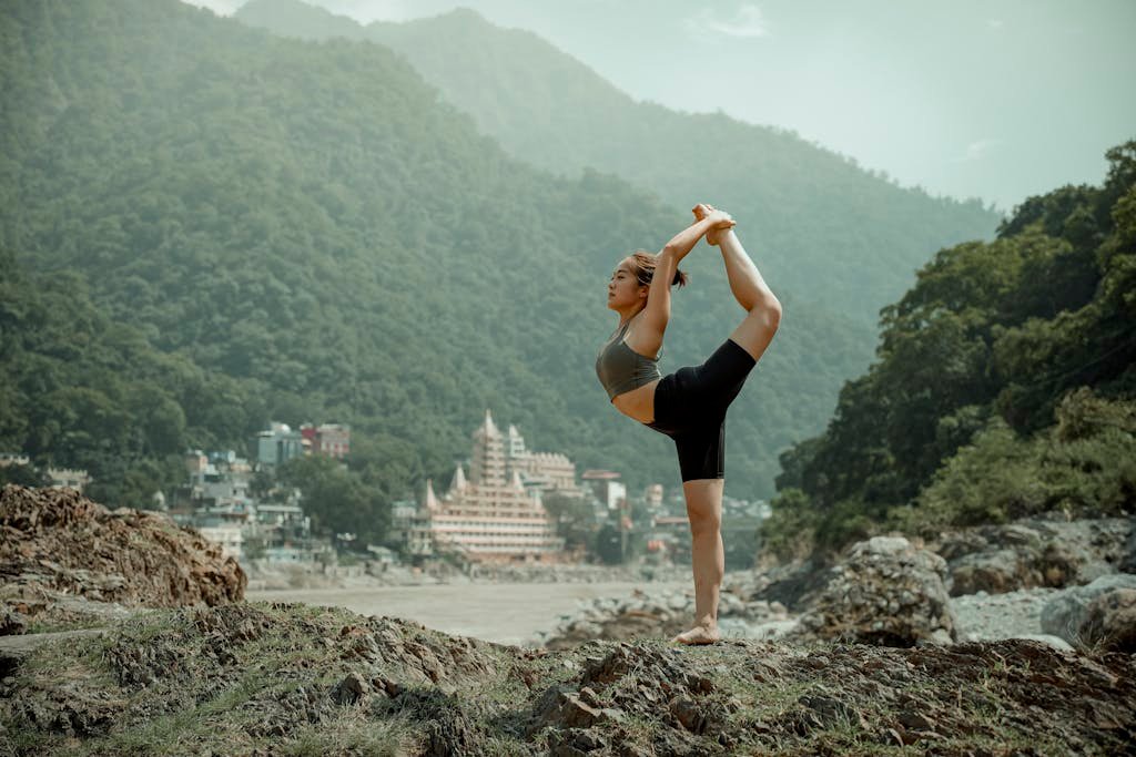 Young woman practicing yoga in Rishikesh with a backdrop of mountains and temples.