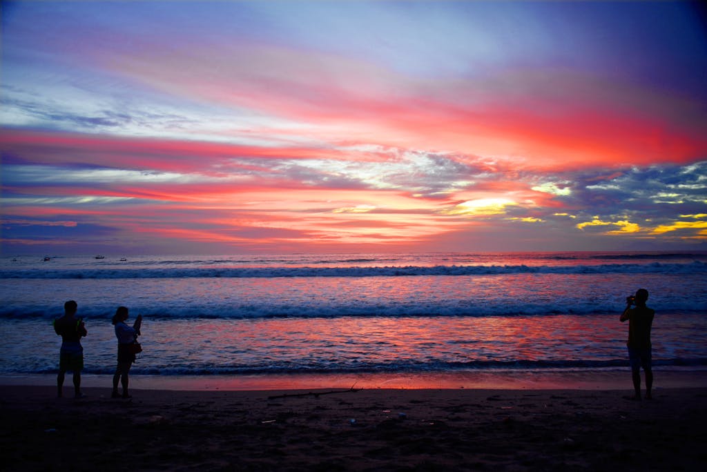 Silhouetted people capturing a stunning sunset over Kuta Beach's vibrant seascape.