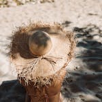 A person wearing a straw hat enjoys sunbathing on a sandy beach, embodying summer vacation vibes.