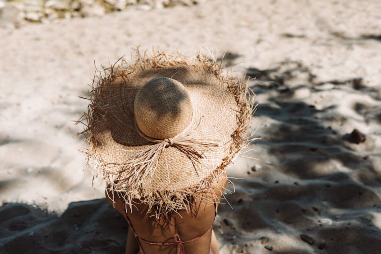 A person wearing a straw hat enjoys sunbathing on a sandy beach, embodying summer vacation vibes.