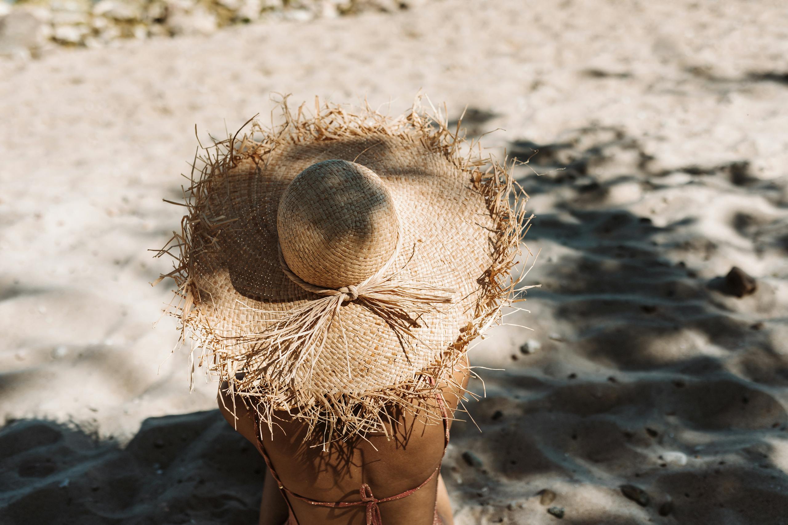 A person wearing a straw hat enjoys sunbathing on a sandy beach, embodying summer vacation vibes.